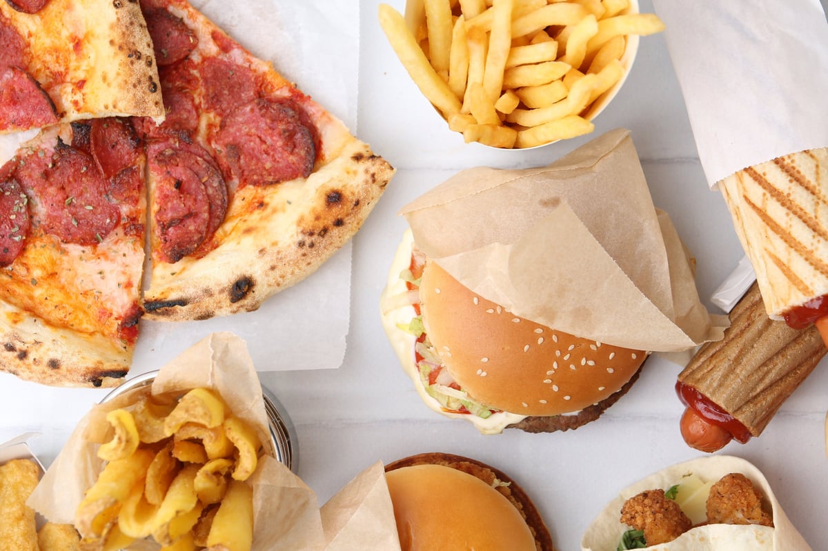 Different delicious fast food on white tiled table
