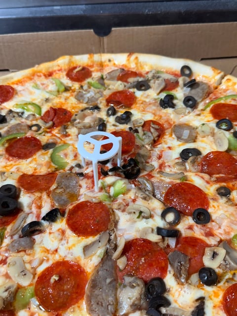 Pizza topped with pepperoni, sausage, mushrooms, black olives, and green peppers in a delivery box